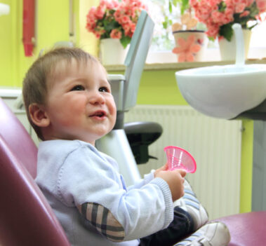 lachendes Kind mit Becher auf Zahnarztstuhl